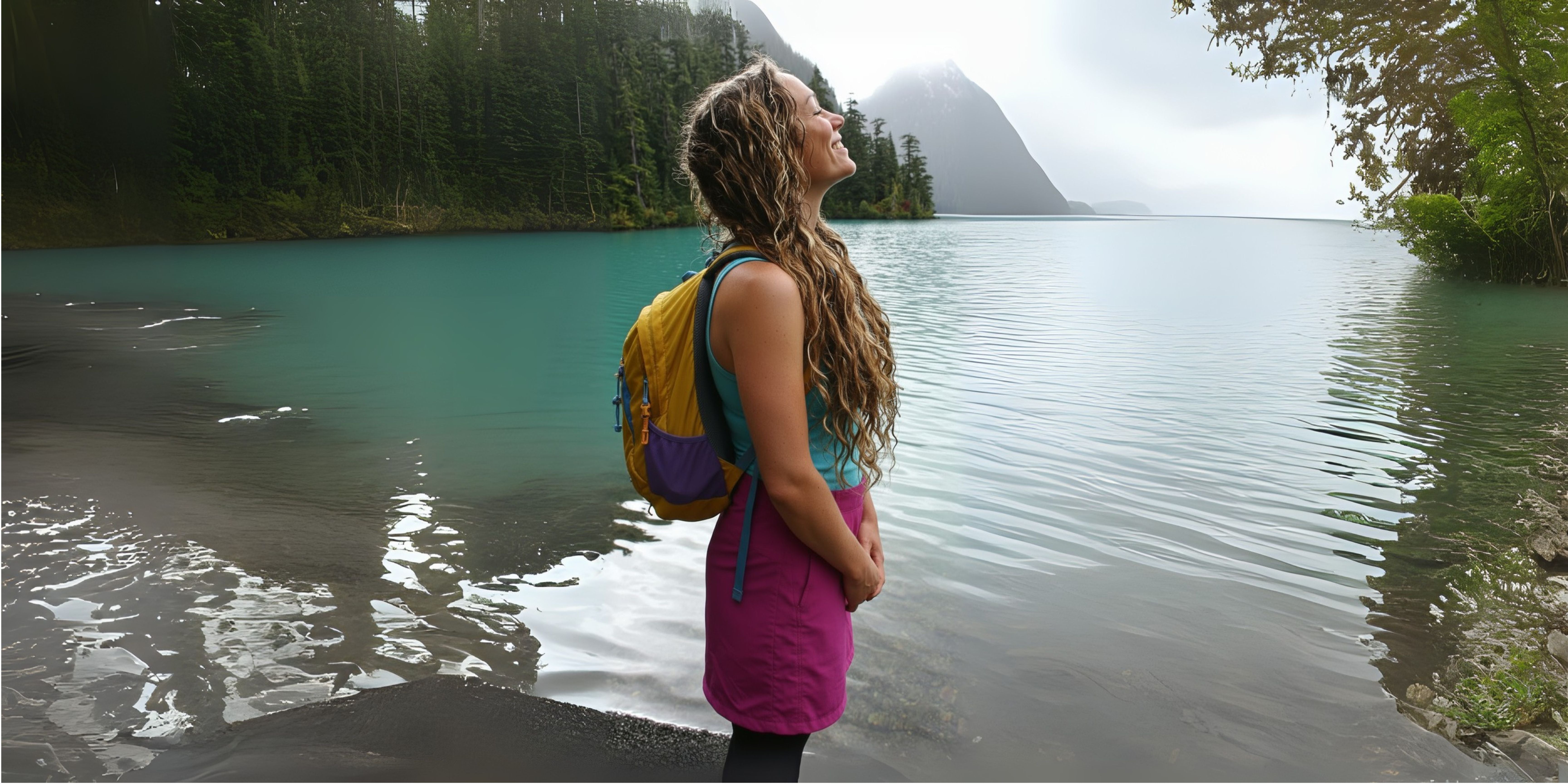 Beautiful woman with wavy hair standing in front of alpine lake looking up at mountains
