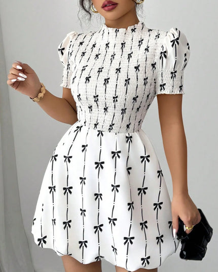 White dress with black bow pattern worn by a person against a gray background