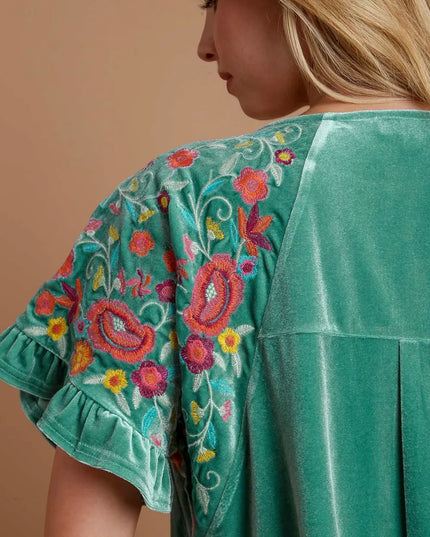 Teal/mint velvet top with floral embroidery on a beige background