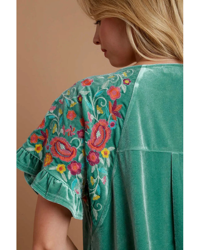 Teal/mint velvet top with floral embroidery on a beige background