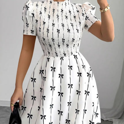 Woman wearing a white dress with black bow pattern, holding a phone.