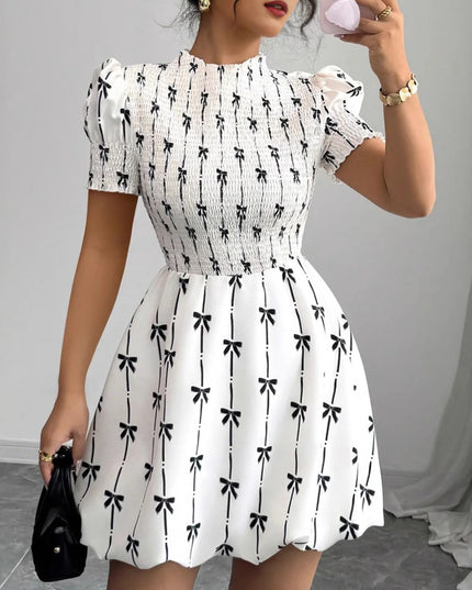 Woman wearing a white dress with black bow pattern, holding a phone.