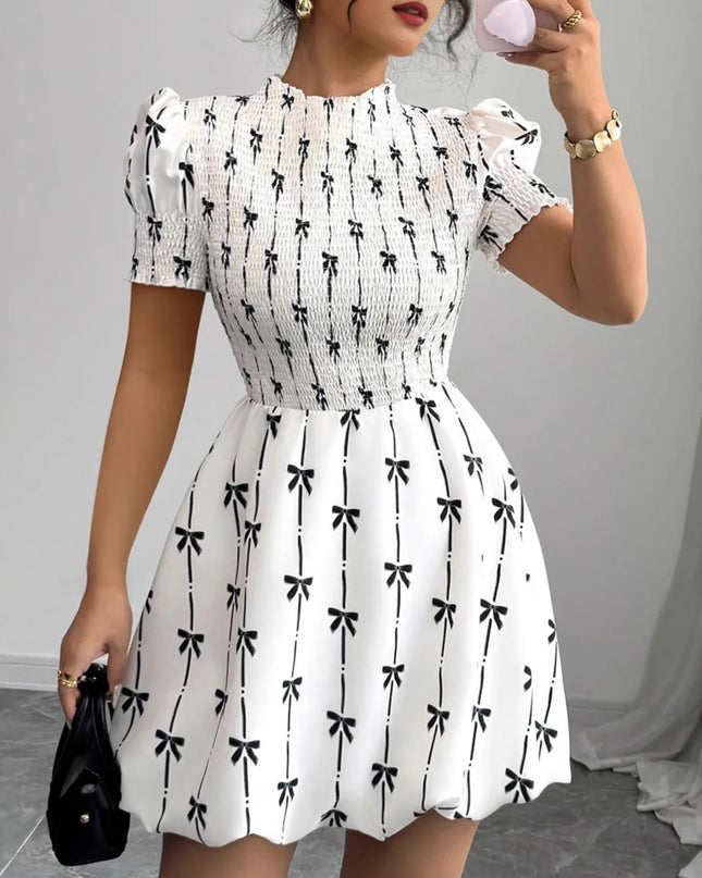 Woman wearing a white dress with black bow pattern, holding a phone.