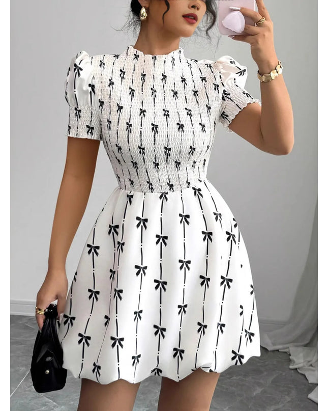 Woman wearing a white dress with black bow pattern, holding a phone.