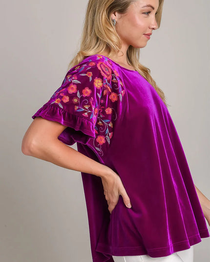 Woman wearing a purple blouse with floral embroidery on a plain background