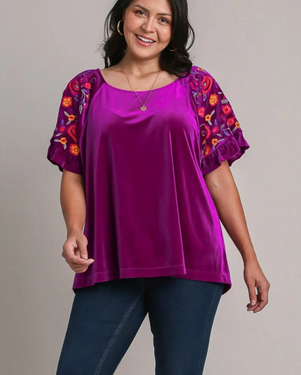 Woman wearing a purple top with colorful sleeves against a gray background