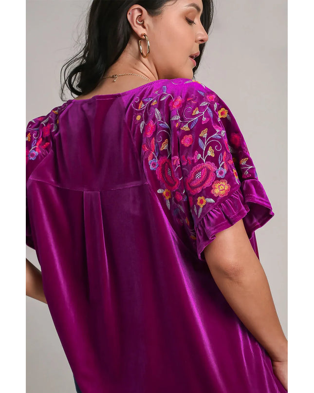 Purple blouse with floral embroidery on sleeves against a neutral background