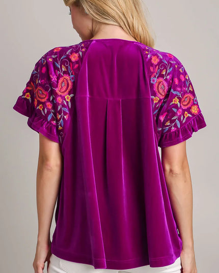 Purple blouse with floral patterns on sleeves worn by a woman, on a neutral background