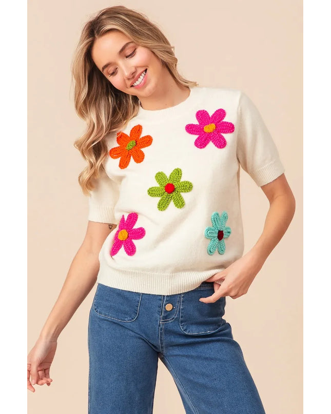 Woman wearing a white sweater with colorful flower patterns on a beige background