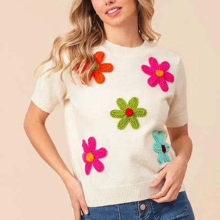Woman wearing a cream sweater with colorful flower patterns on a beige background