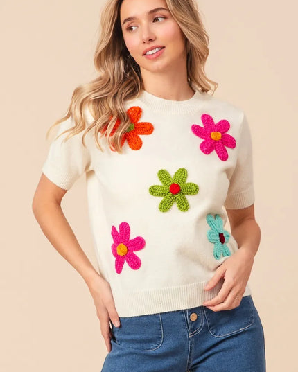 Woman wearing a cream sweater with colorful flower patterns on a beige background