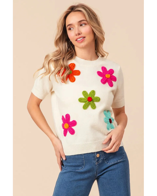 Woman wearing a cream sweater with colorful flower patterns on a beige background