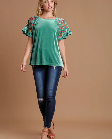 Woman wearing a green top with colorful sleeves and blue jeans on a brown background