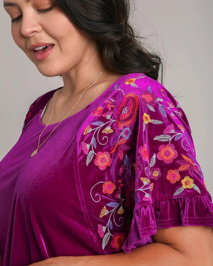 Woman wearing a purple top with floral embroidery on a plain background