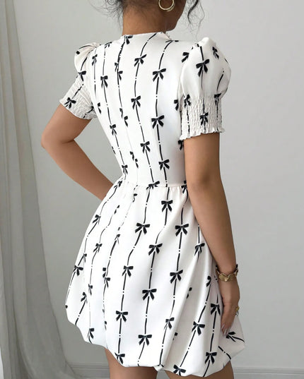 White dress with black bow pattern worn by a person against a plain background