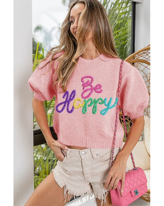 Woman wearing a pink sweater with 'Be Happy' text, standing outdoors.