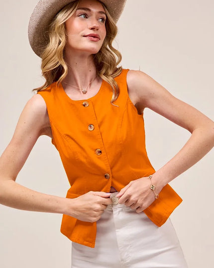 Woman wearing an orange vest and white pants with a beige hat on a plain background