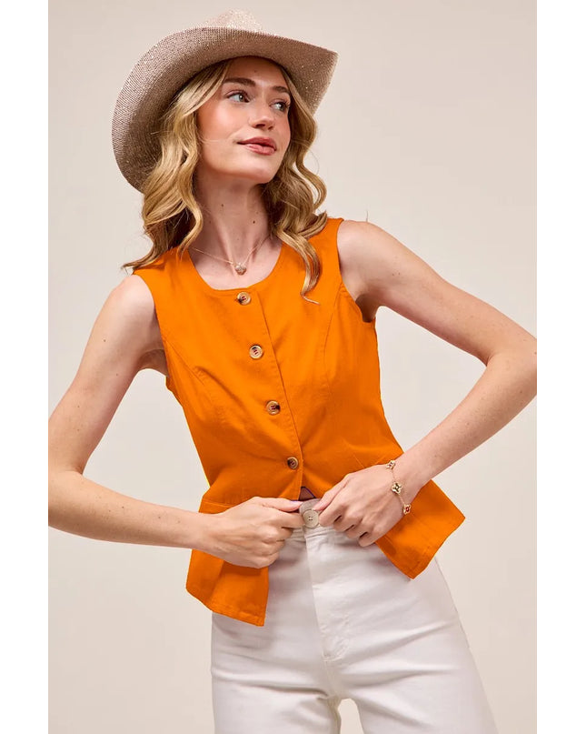 Woman wearing an orange vest and white pants with a beige hat on a plain background