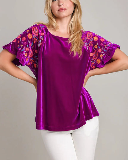 Woman wearing a purple top with floral sleeves on a plain background