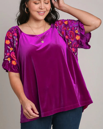 Woman wearing a purple blouse with floral sleeves against a neutral background
