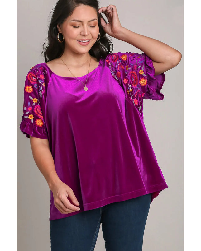 Woman wearing a purple blouse with floral sleeves against a neutral background
