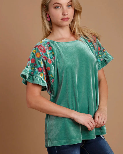 Woman wearing a green top with floral embroidery on a brown background