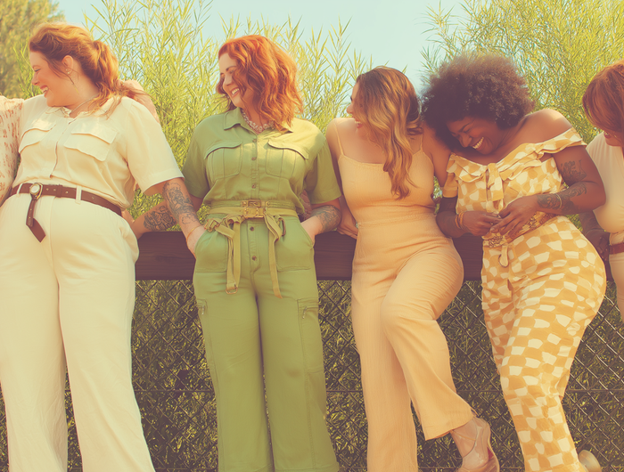 Group of diverse women in stylish jumpsuits and outfits laughing together outdoors, representing inclusivity in fashion.